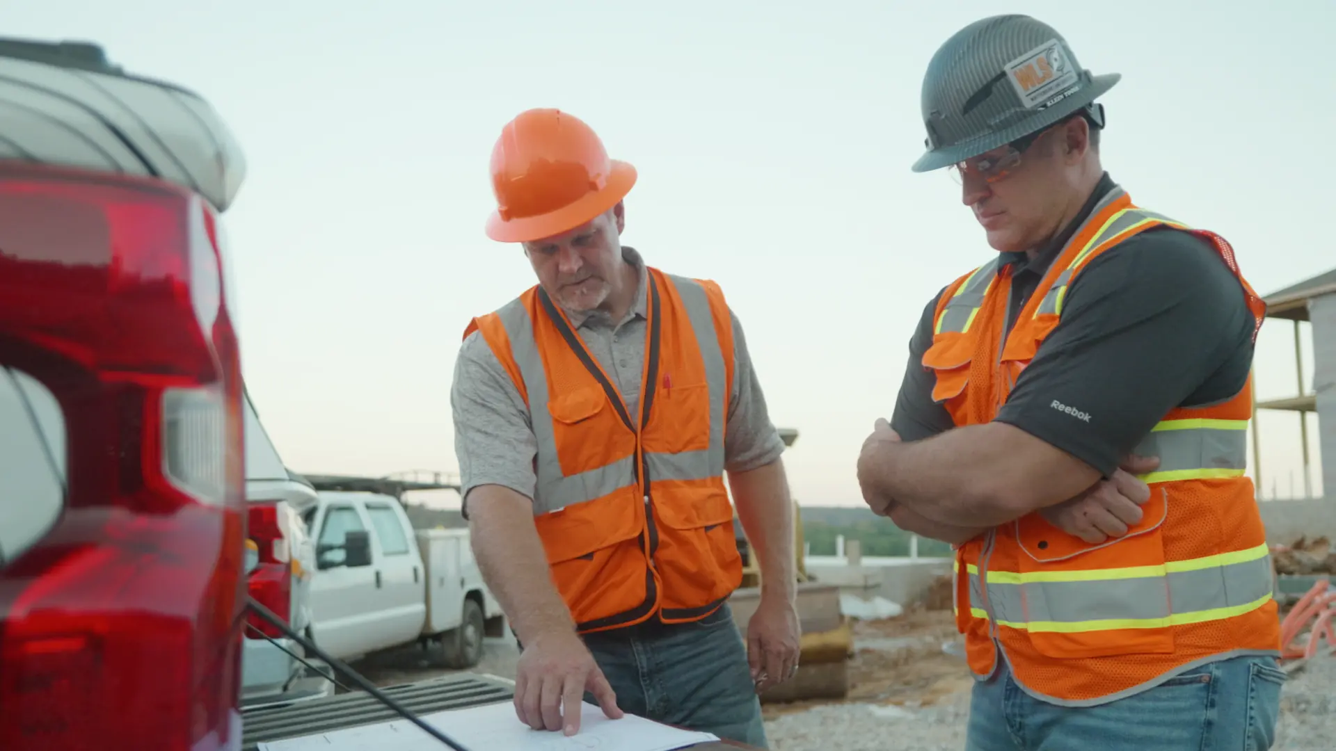 Two Utility Locators technicians in hi-vis gear and hard hats at a job site near their truck