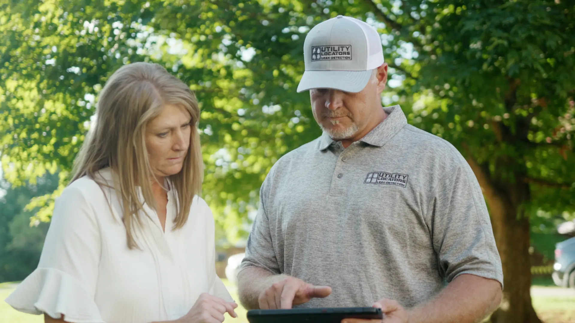 Utility Locators technician wearing a company cap talking with a homeowner outdoors
